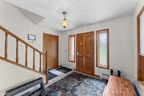 A room with a wooden staircase, a door with a window, a radiator, and a patterned rug.