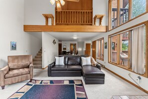 A spacious living area with a large sectional sofa, a leather armchair, and a colorful rug. A wooden staircase leads to an upper level.