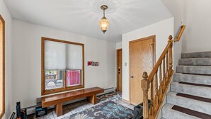 A hallway with a bench, a wooden door, a staircase, and a patterned rug.