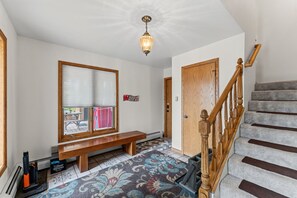 A hallway with a bench, a wooden door, a staircase, and a patterned rug.