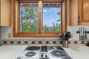 A kitchen with a double window, two stovetops, and a knife rack. - Red Bird Retreat | Arctic Hot Tub | Stunning Views (Silverthorne)
