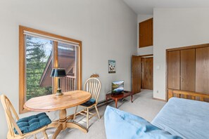 A room with a wooden table, a chair, a bed, a television, and a door. - Red Bird Retreat | Arctic Hot Tub | Stunning Views (Silverthorne)
