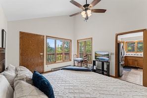 A bedroom with a bed, a ceiling fan, and a view of the outdoors through large windows.