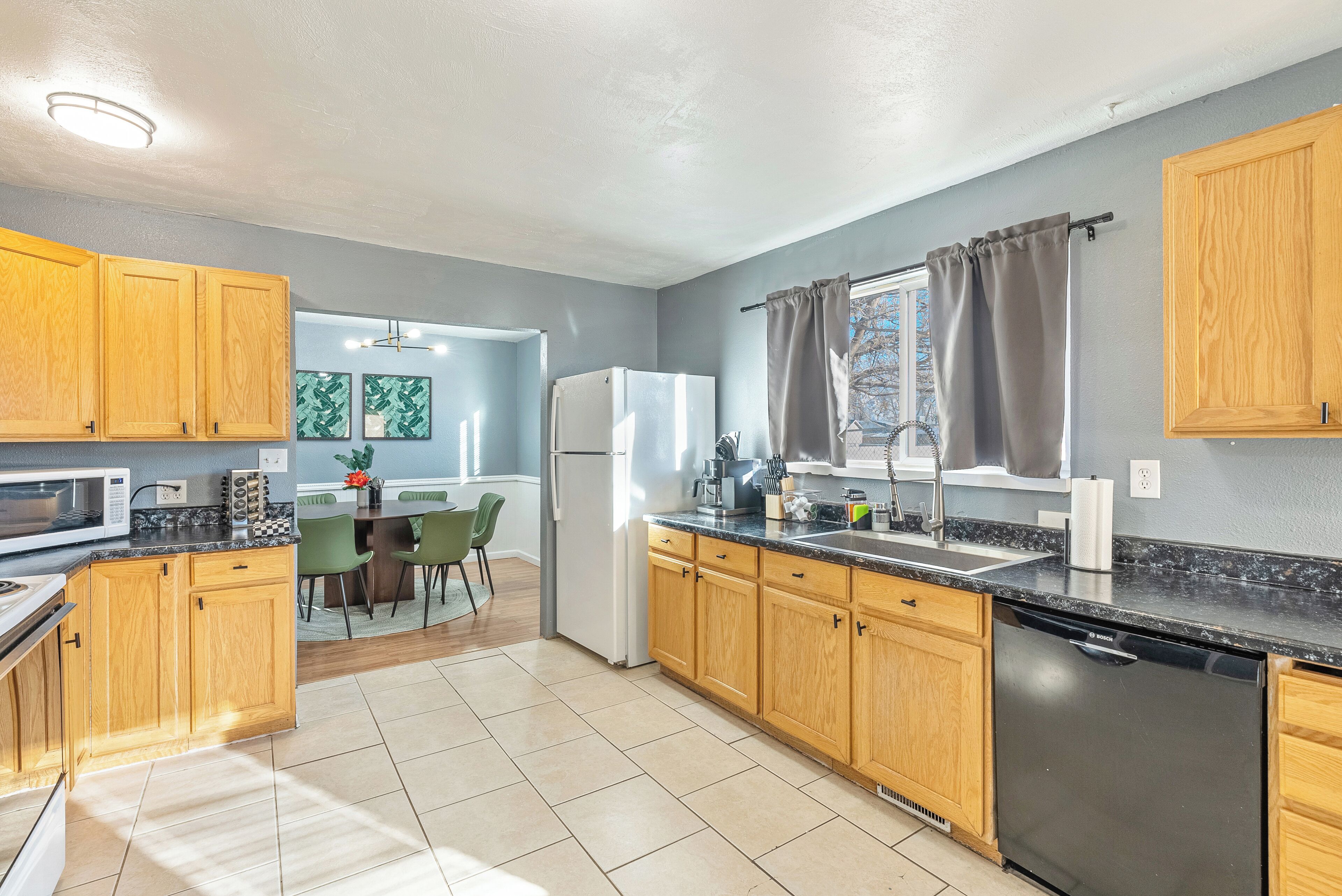 A modern kitchen with wooden cabinets, a black countertop, and a Bosch dishwasher.