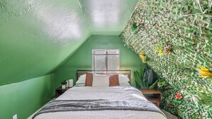 A room with a sloped ceiling, a bed with white bedding, a nightstand with a lamp, and a wall with a green leafy pattern.