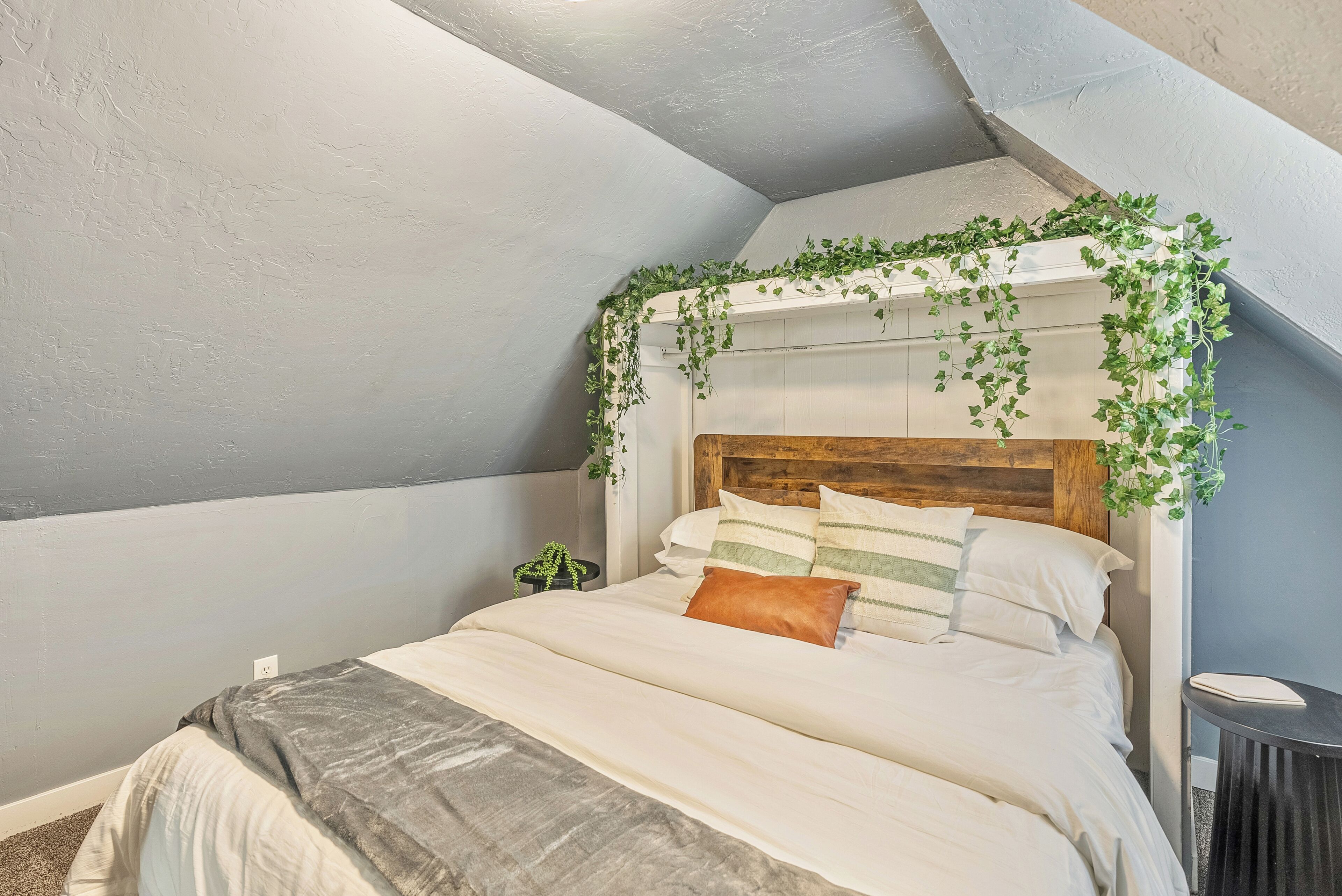 A bedroom with a sloped ceiling, a wooden headboard, and a bed with white bedding and decorative pillows.