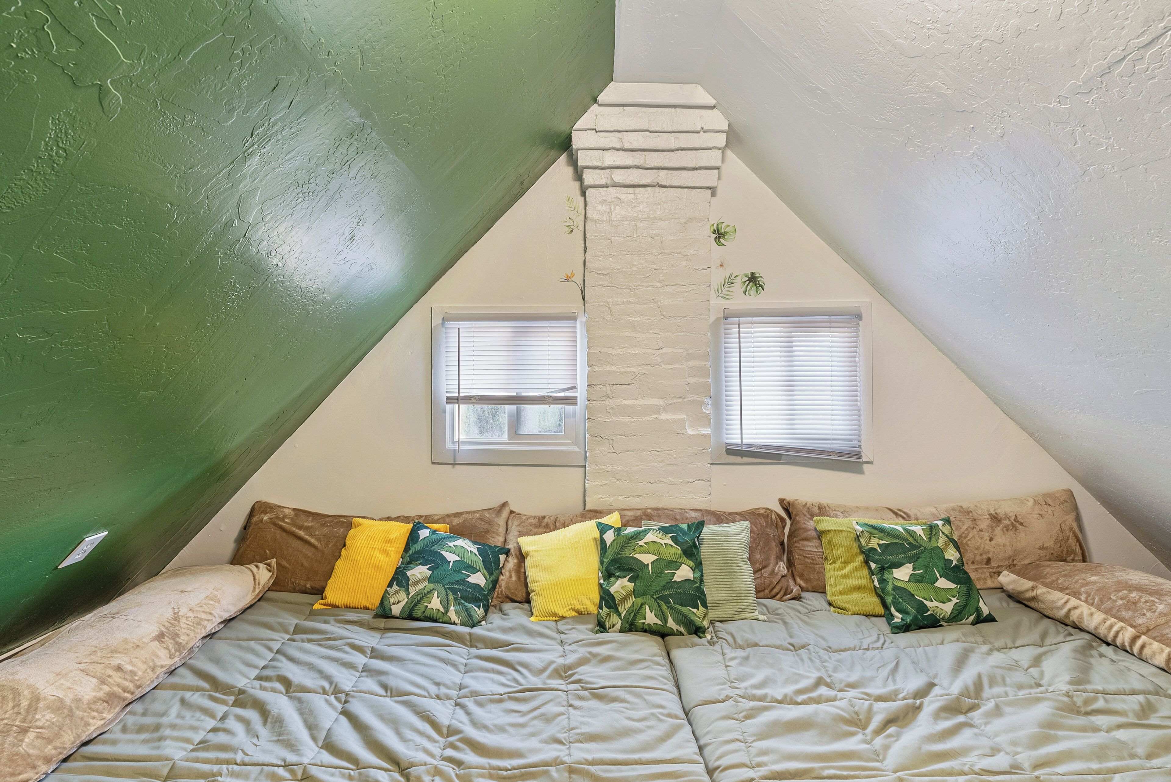 Une chambre avec un plafond en pente, deux fenêtres, un lit avec de nombreux oreillers et un mur vert.