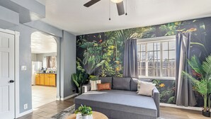 A living room with a grey sofa, a coffee table, and a large jungle-themed mural on the wall.