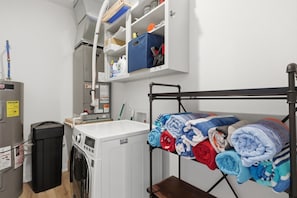 A compact laundry area with a washing machine, a drying rack, and a small cabinet with storage items. - The Golden Hour - Elevator & Main Channel Views! (Osage Beach)