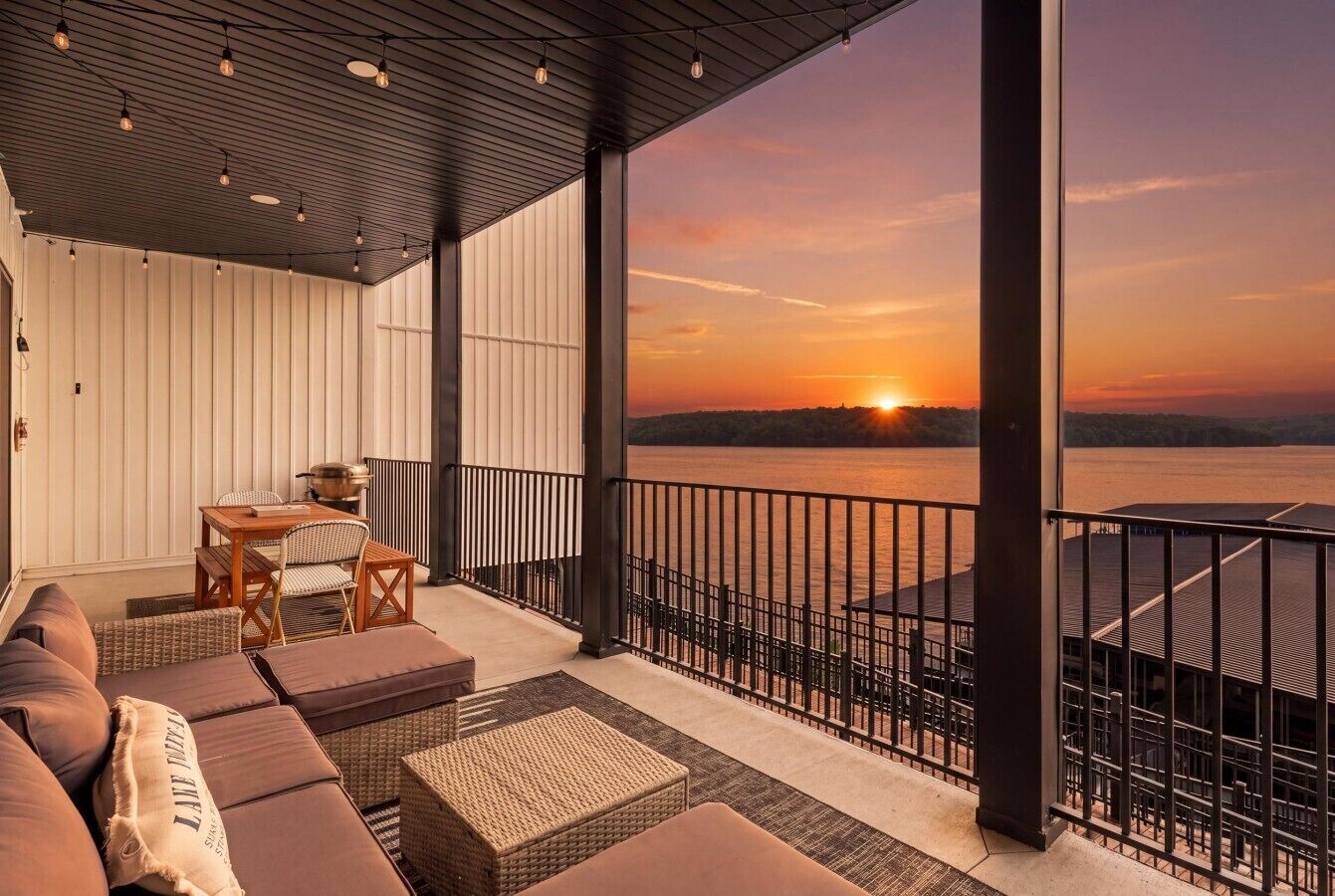 Un balcon offrant une vue sur le coucher de soleil sur l’eau, aménagé avec un canapé, des fauteuils et une table.