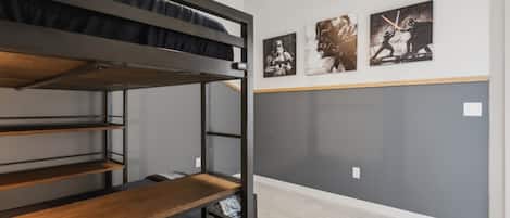 Una cama litera con un estante de madera, una pared gris con obras de arte y un suelo alfombrado.