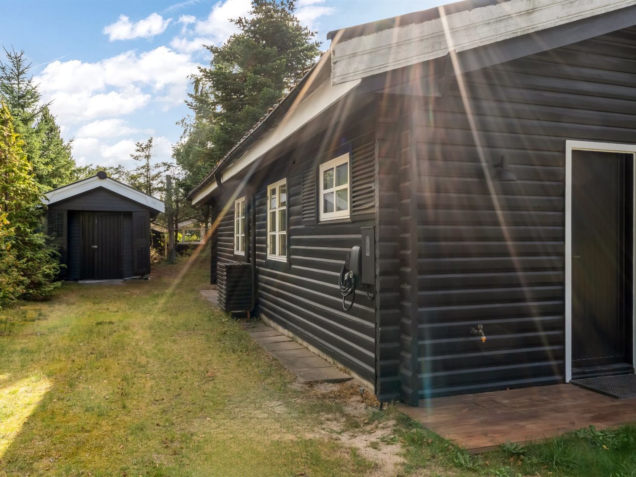 A wooden cabin with a garage, a small shed, and a grassy yard.