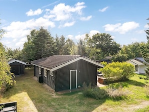 A small, dark-colored wooden cabin with a sloped roof, surrounded by a grassy yard and dense trees. - "Andrina" - 350m from the sea by Interhome (Sæby)
