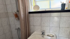 Kylpyhuone, jossa on valkoinen pesuallas, suihku ja ikkuna, josta on näkymä.