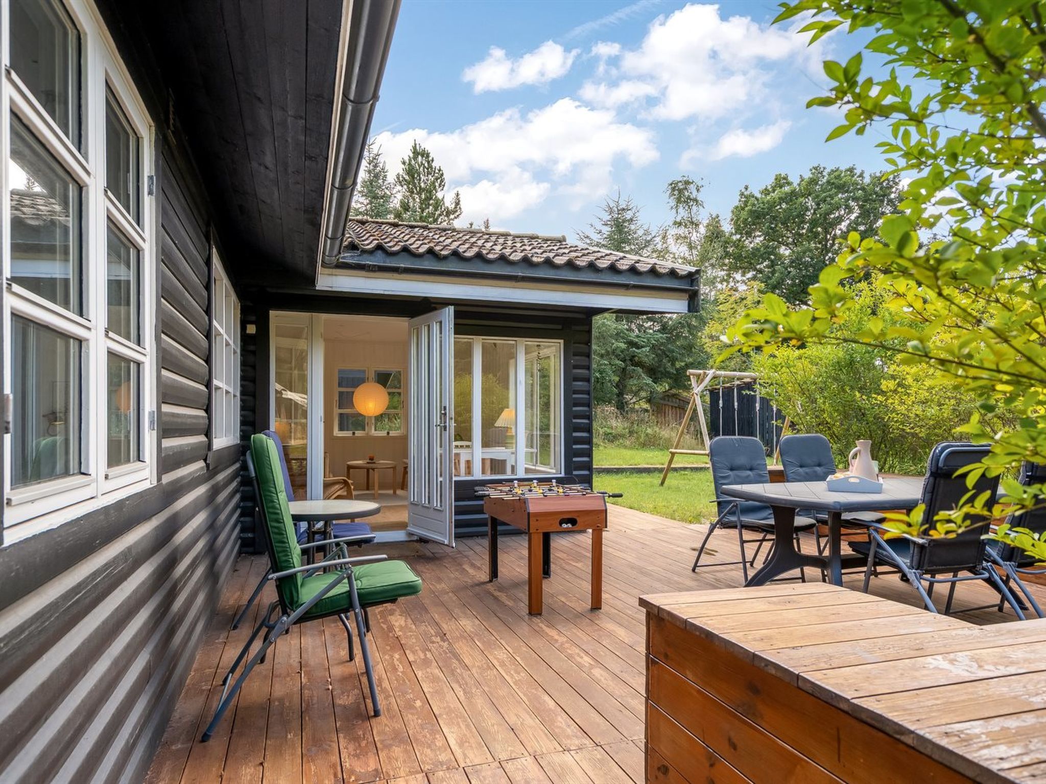A wooden deck with a table and chairs, a foosball table, and a small covered area with a table and chairs.