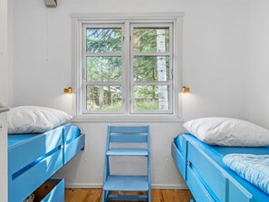 Ein Zimmer mit zwei Etagenbetten, einem Fenster mit Blick auf Bäume und einem Stuhl in der Mitte.