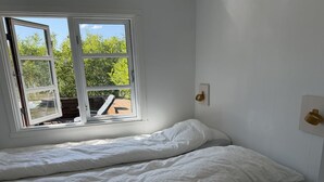 Huone, jossa on sänky, ikkuna ja seinään kiinnitetty valaisin.