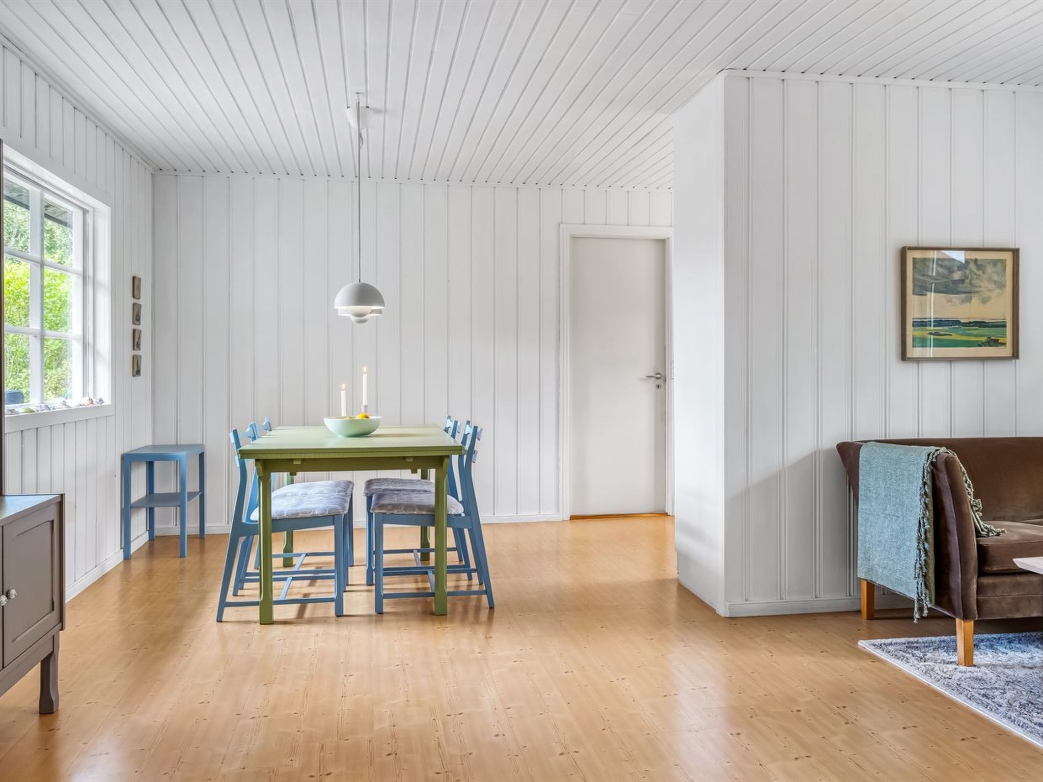 A dining area with a table and chairs, a pendant light, a door, and a framed picture on the wall.