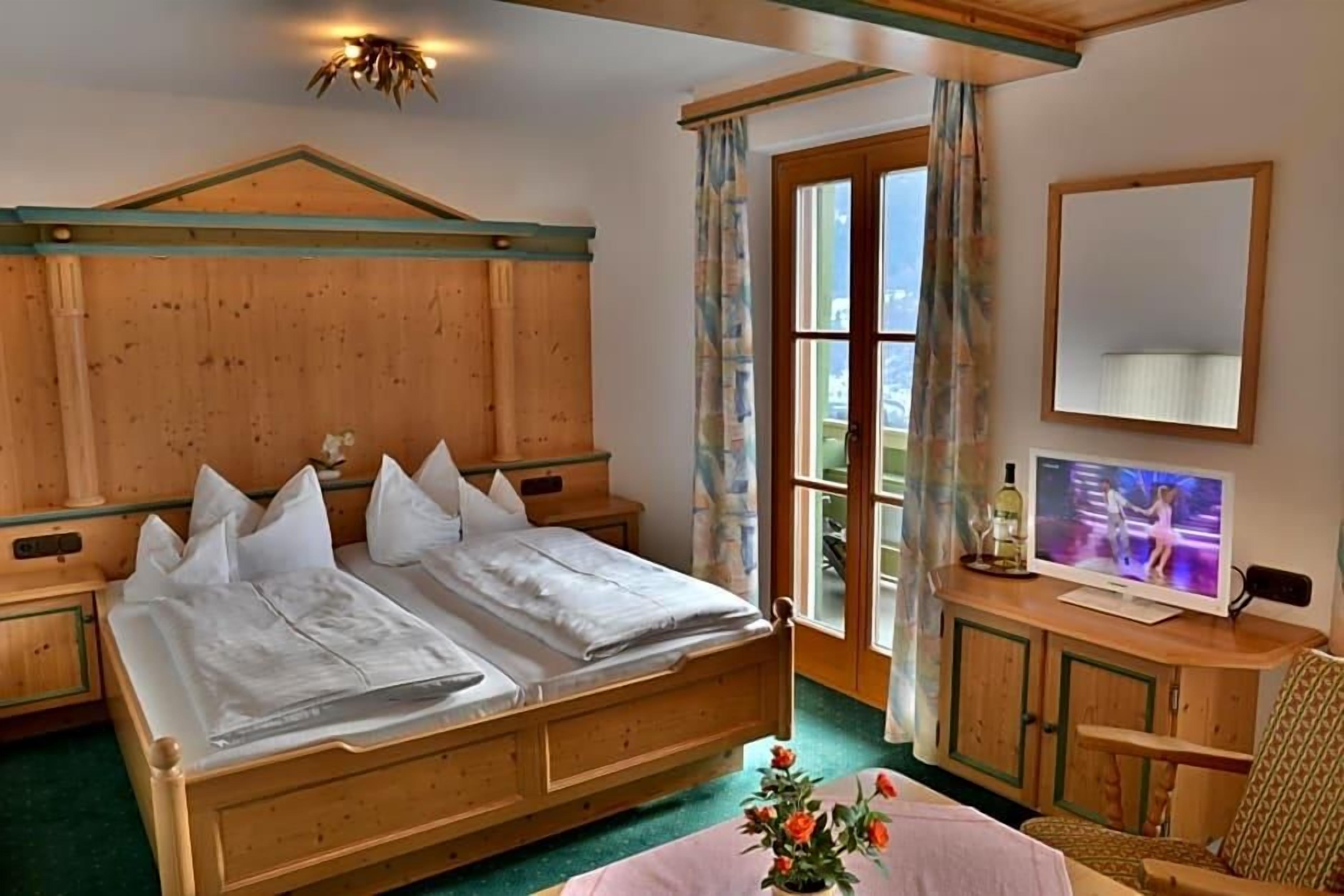 Ein Bett mit Holzbettgestell und Kissen, ein Fernseher auf einer Holzkommode und ein Fenster mit Vorhängen.