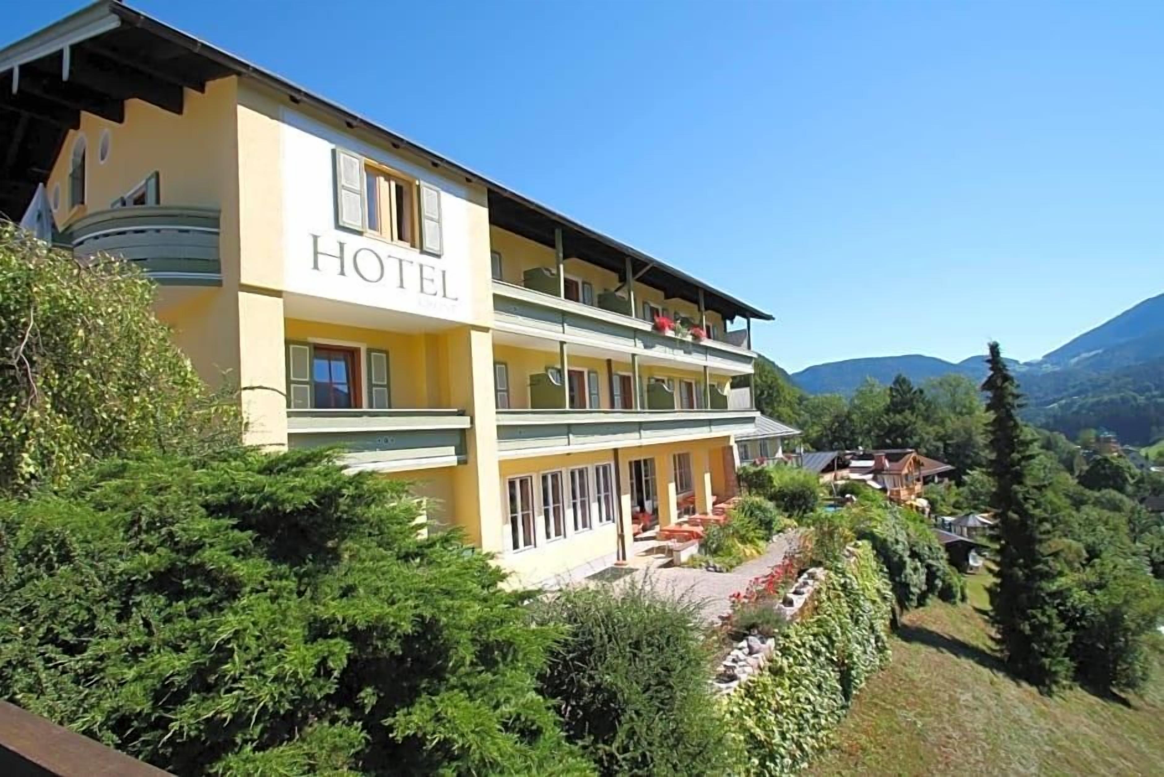 Ein Hotel mit Balkon, umgeben von Grün und Bergen im Hintergrund.