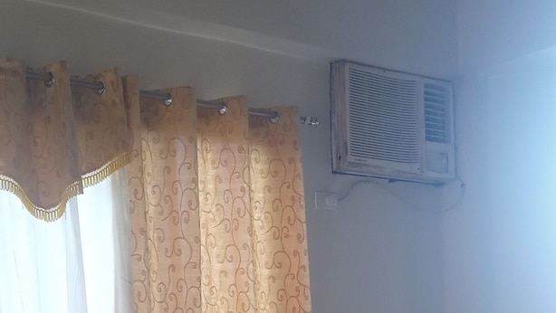 Quarto de hotel padrão com uma cama de solteiro, mesa de cabeceira, ar condicionado e cortinas.