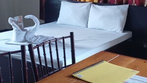 Quarto de hotel com cama, mesa de madeira e janela com cortinas estampadas.
