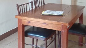 Uma área de refeições com mesa e cadeiras de madeira, luminária no teto e um suporte de metal preto na parede.
