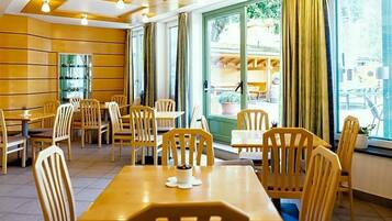 A restaurant with wooden tables and chairs, large windows with curtains, and a view of the street outside.