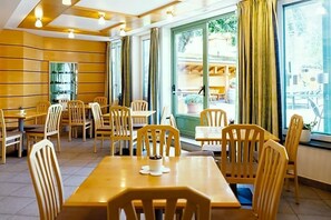 A restaurant with wooden tables and chairs, large windows with curtains, and a view of the street outside. - Wandergasthof Stern (Funes)