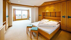 A hotel room with a large bed, wooden headboard, and a balcony view. - Wandergasthof Stern (Funes)