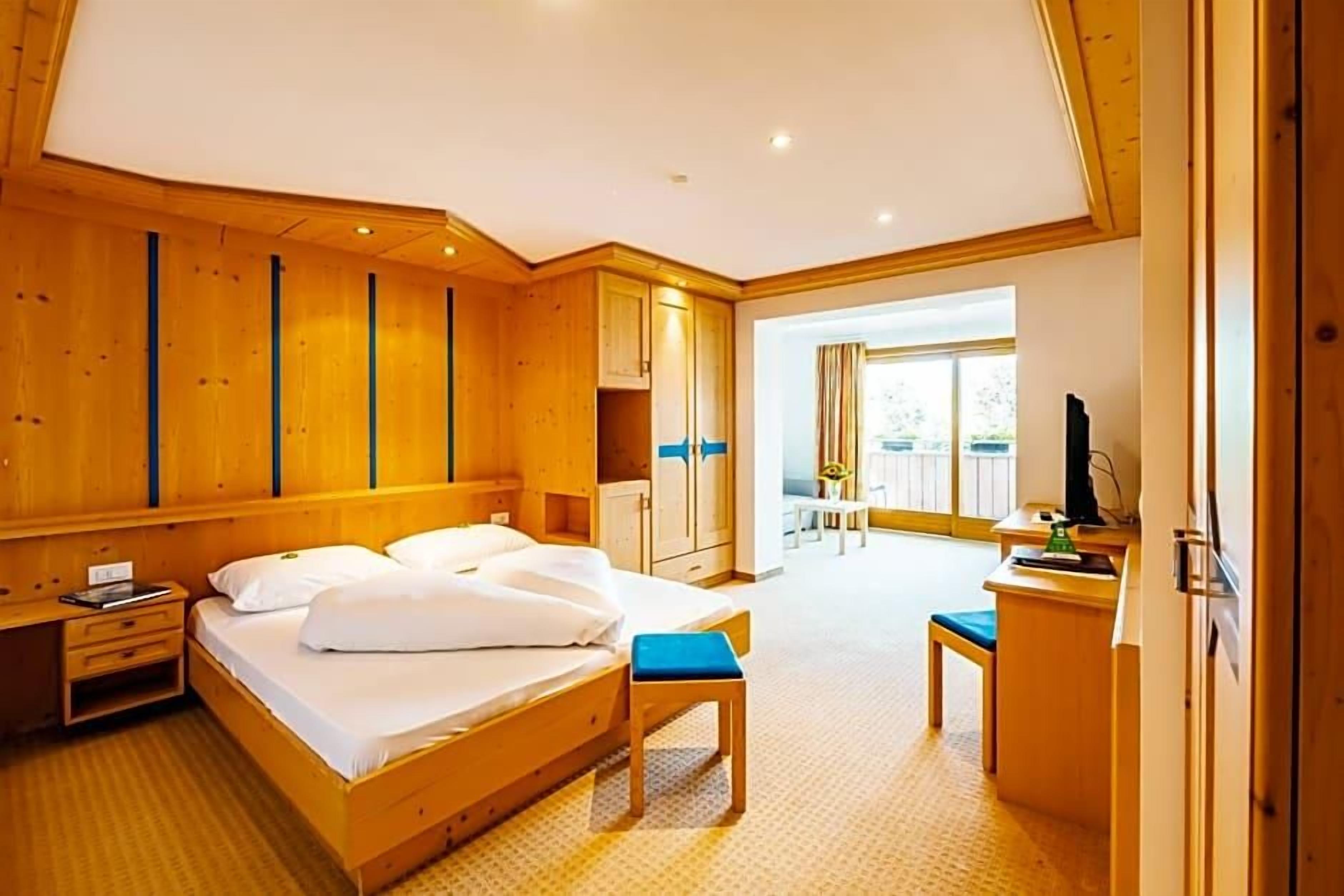 A hotel room with a wooden bed, a desk, a chair, and a view of the outdoors.