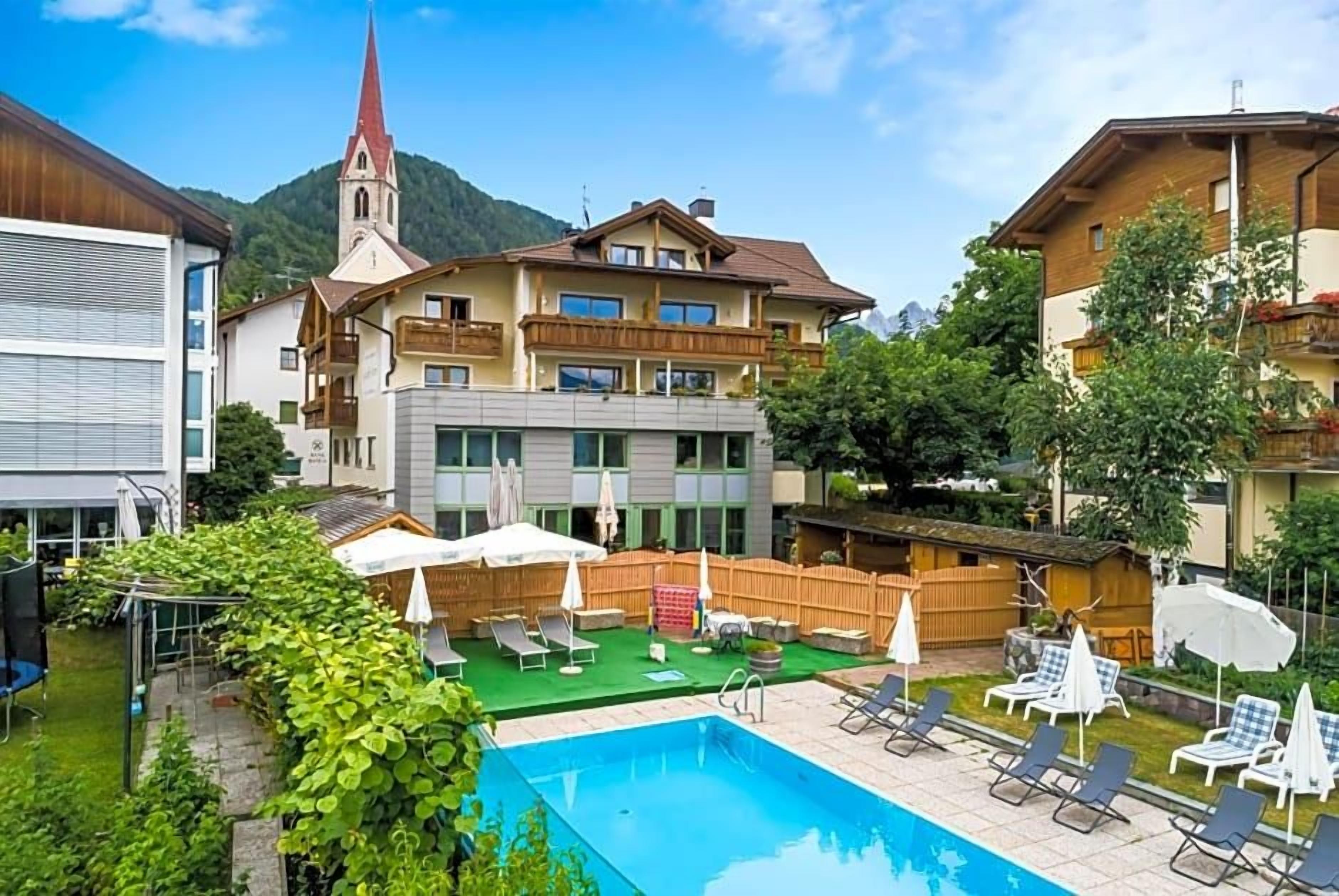Un edificio residencial con piscina, mobiliario exterior y una iglesia al fondo.