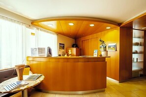 A reception area with a curved wooden counter, a seating area with a table, and a window with curtains. - Wandergasthof Stern (Funes)