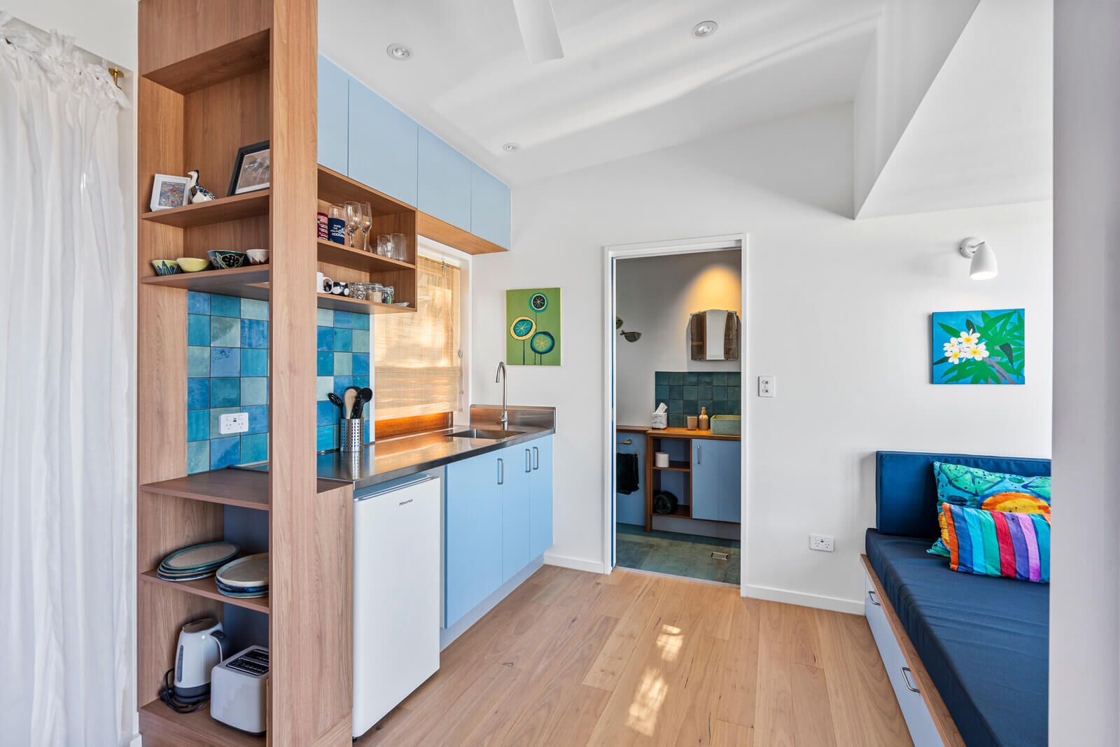 A compact kitchen with blue cabinets, a dishwasher, and a countertop with various items.