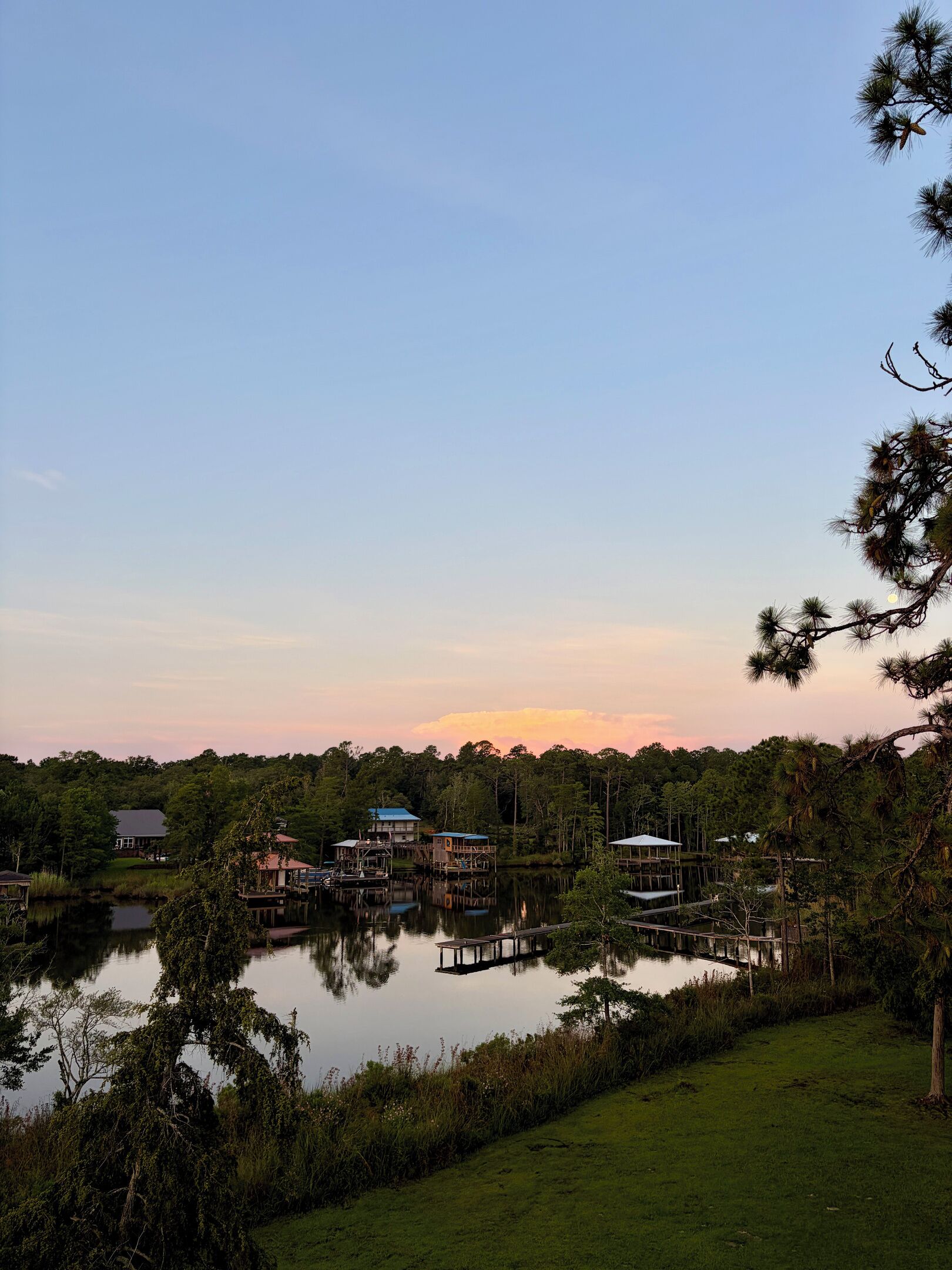 Une propriété au bord du lac, avec plusieurs bateaux amarrés, une zone herbeuse et divers bâtiments, dont une maison et une construction dotée d’un toit bleu.