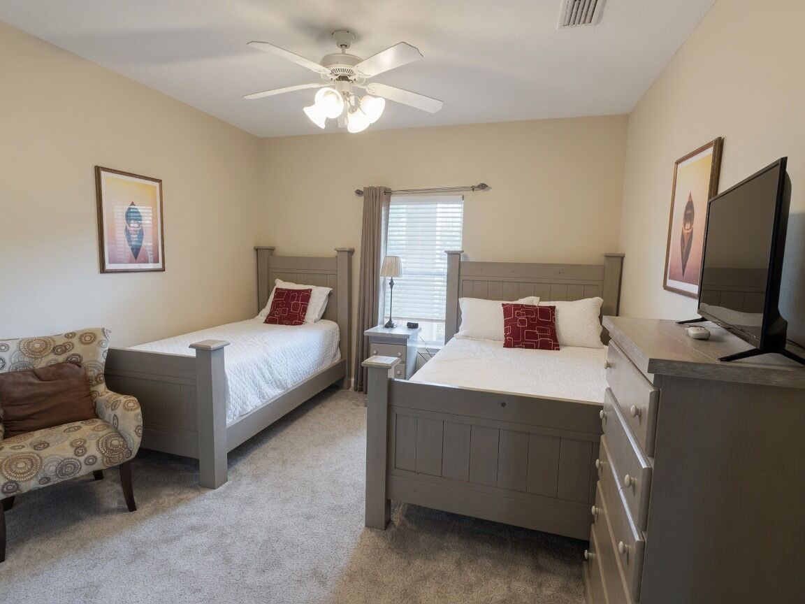 Une chambre avec deux lits simples, un bureau, une chaise, une télévision et un ventilateur de plafond.