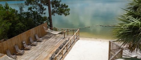 A wooden deck with lounge chairs and a hammock overlooking a calm lake.