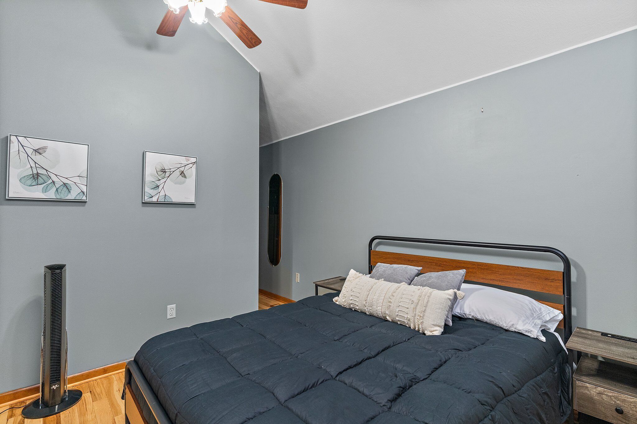 A bedroom with a bed, a ceiling fan, and two wall-mounted artworks.