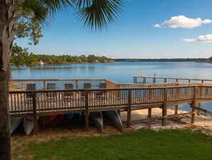 A wooden deck with chairs and tables overlooking a calm lake, surrounded by greenery. - Waterfront Condo w/ Boat Docking & Fishing (Foley)