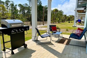 Ein Außenbereich mit Terrasse, Grill, Stühlen und Blick auf einen angelegten Garten.