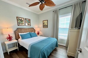 Ein Hotelzimmer mit einem Bett, zwei Nachttischen, einem Deckenventilator und Kunstwerken an den Wänden.