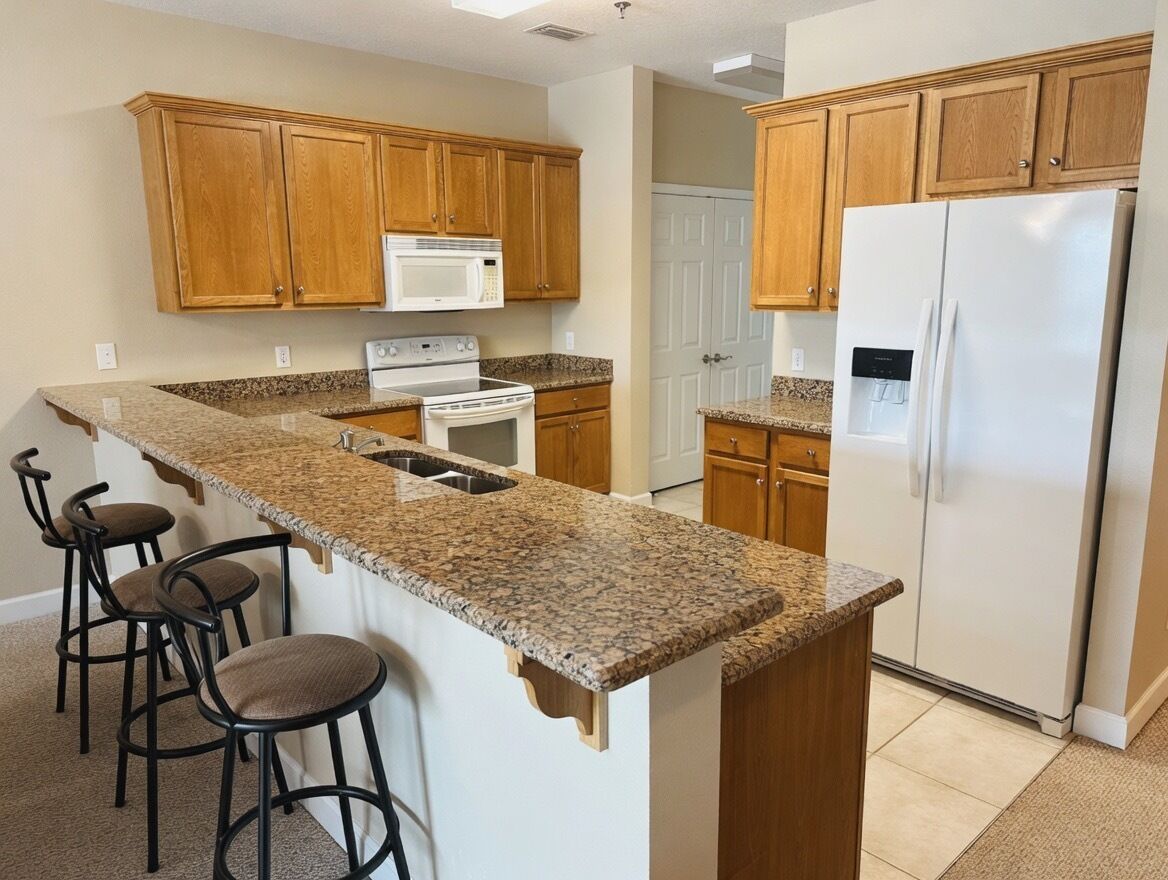 A kitchen with wooden cabinets, a granite countertop, a white refrigerator, a stove, and a microwave.