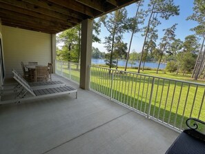 Ein überdachter Außenbereich mit Tisch und Stühlen, einer Rampe und Blick auf einen See und eine Rasenfläche.