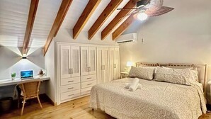 Un dormitori amb sostre inclinat, bigues de fusta, un llit amb estenari estampat, un escriptori amb un ordinador i una cadira.