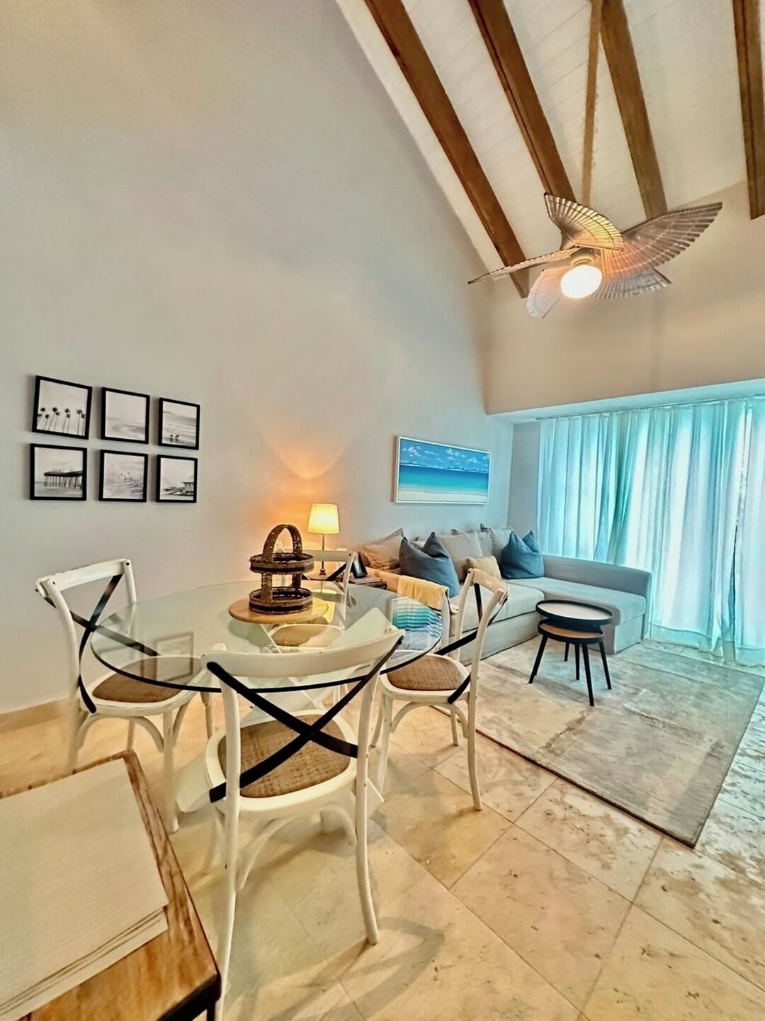 A modern living room with a glass dining table, white chairs, a sofa, and a ceiling fan.