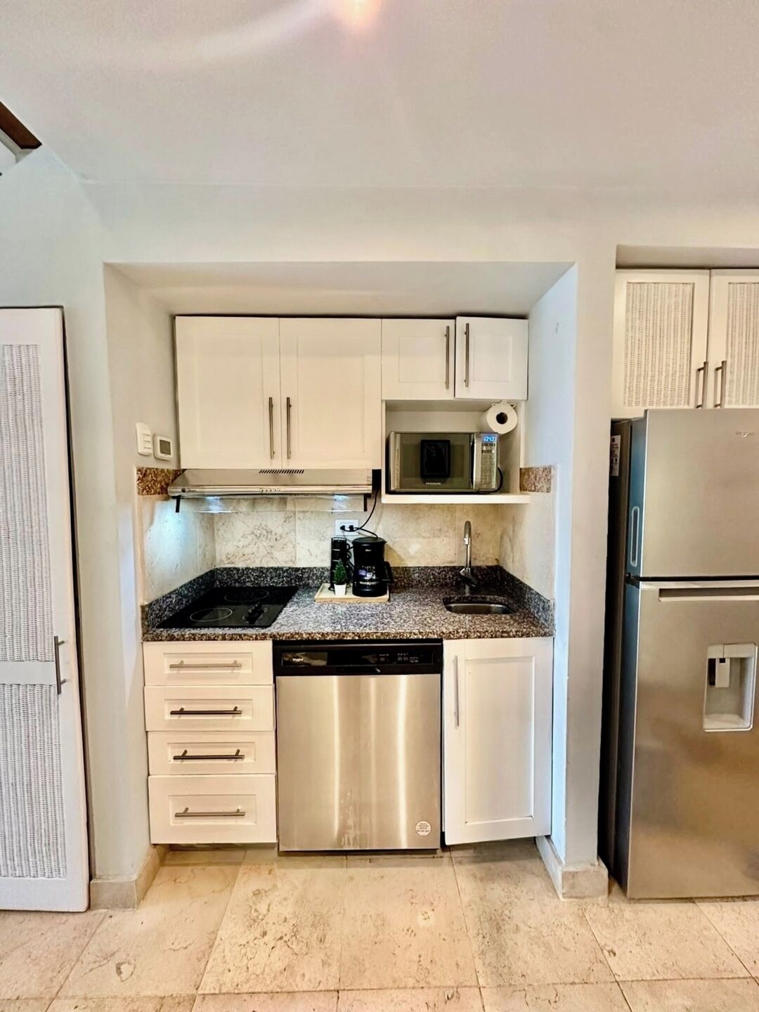 A compact kitchen with white cabinets, a stainless steel dishwasher, a microwave, and a refrigerator.