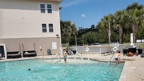 Una piscina con agua cristalina, un área de descanso con sillones, y un edificio al fondo.