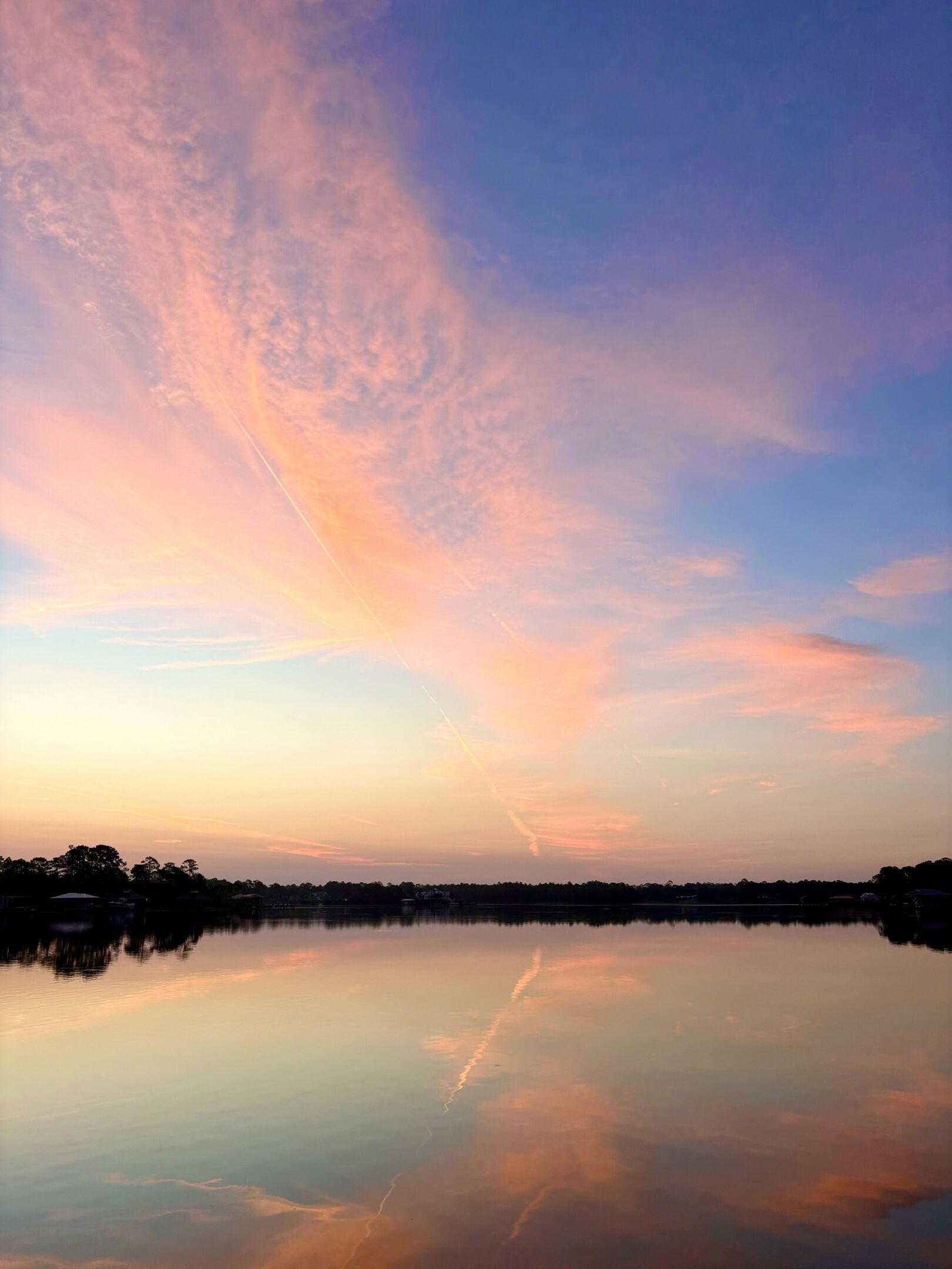 Un lago tranquillo che riflette il cielo al tramonto, con una scia di condensazione visibile.