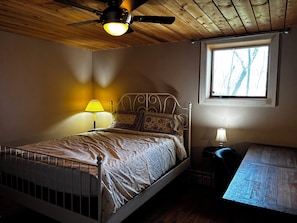 A bedroom with a bed, a window, a ceiling fan, and a small table.