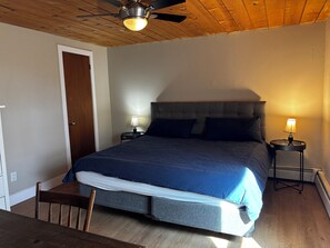 A bedroom with a bed, two bedside tables with lamps, a ceiling fan, and a wooden door.